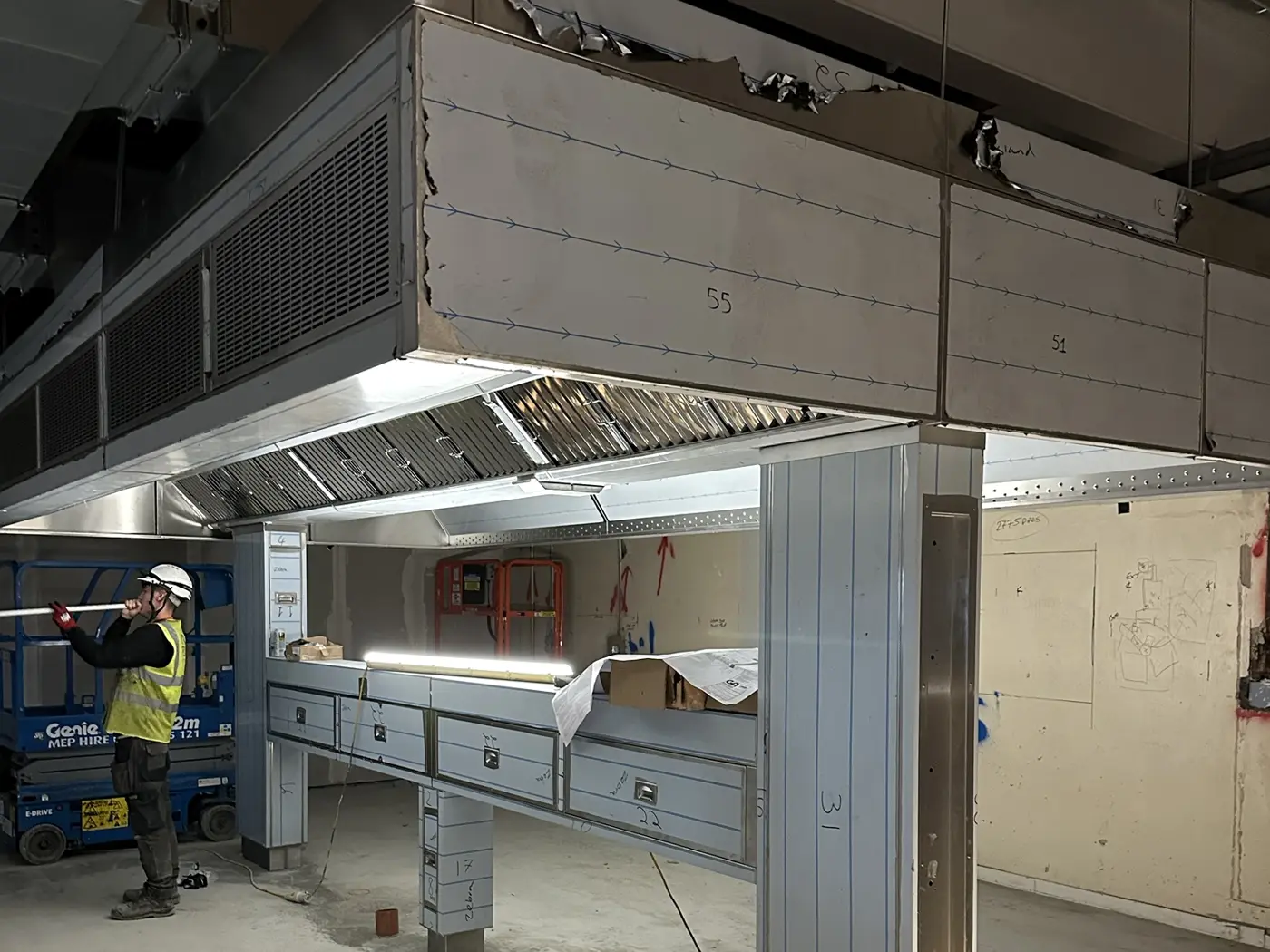 REAL Ventilation installer fitting lighting to a large island canopy with supply air grilles on a commercial kitchen site