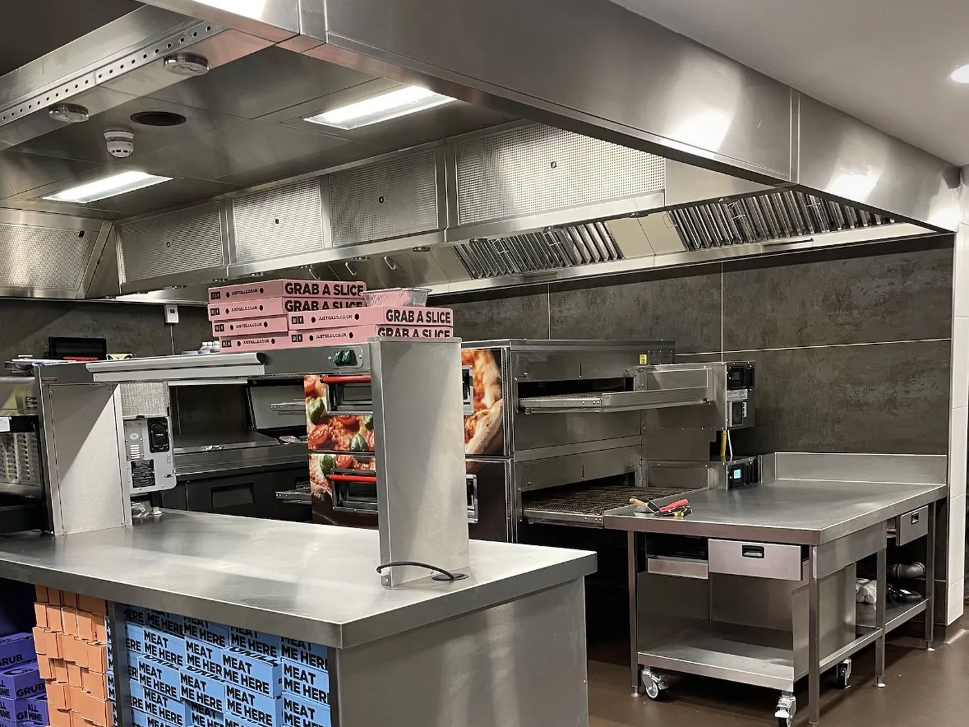 Stainless steel L-shaped canopy and ventilated ceiling over conveyor pizza ovens in the delivery kitchen at Gills, Peterlee