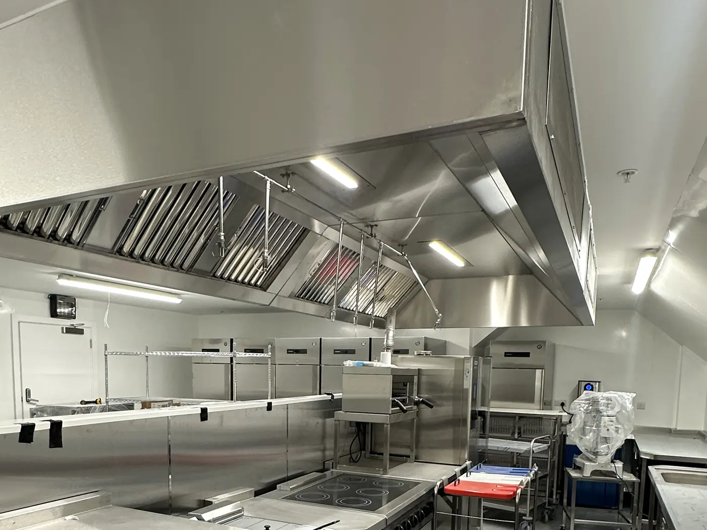 Large stainless steel canopy with baffle filters and lighting above the cooking line in a care home kitchen