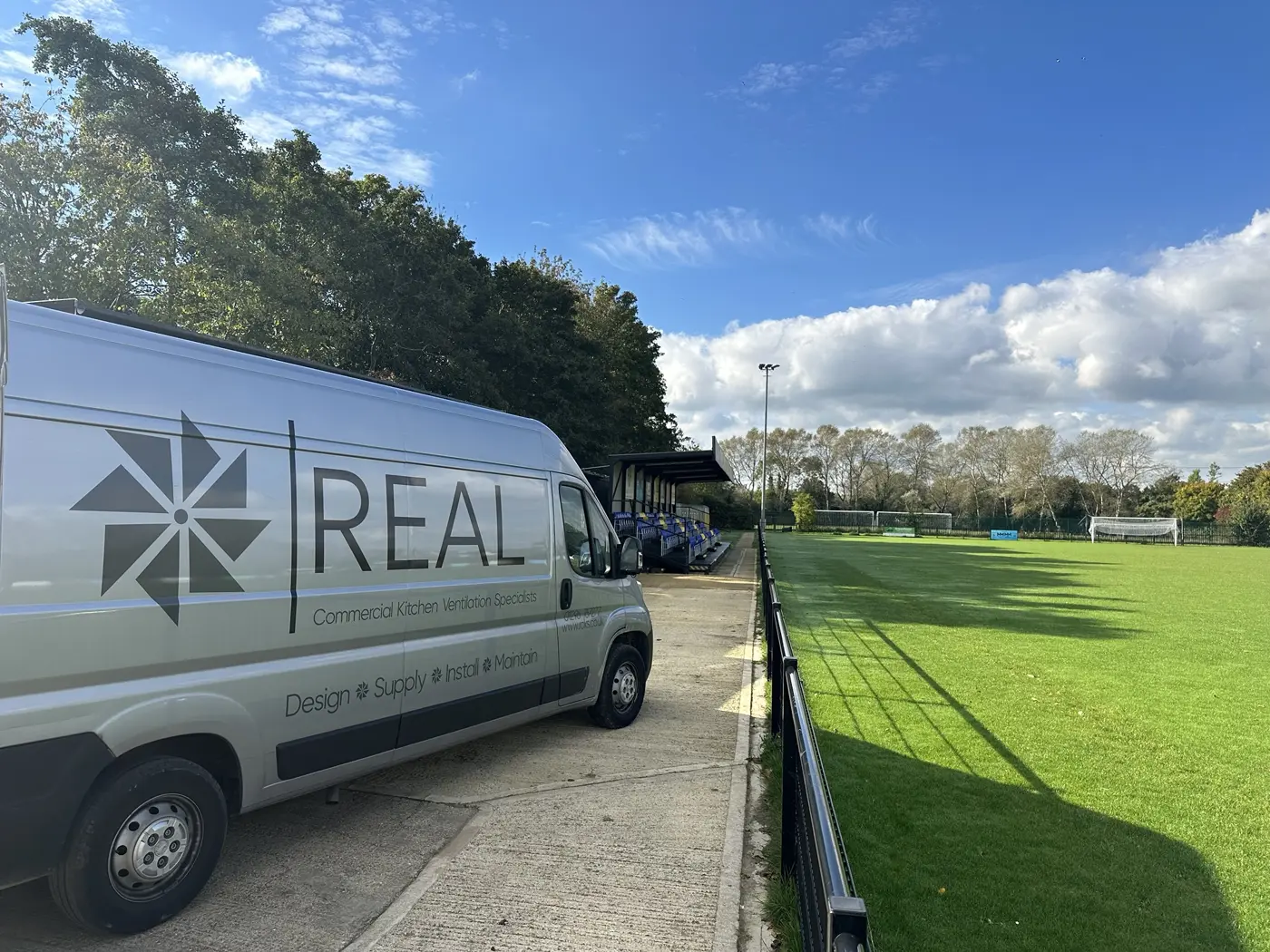 REAL Ventilation site team van parked beside a football pitch and stand on a job