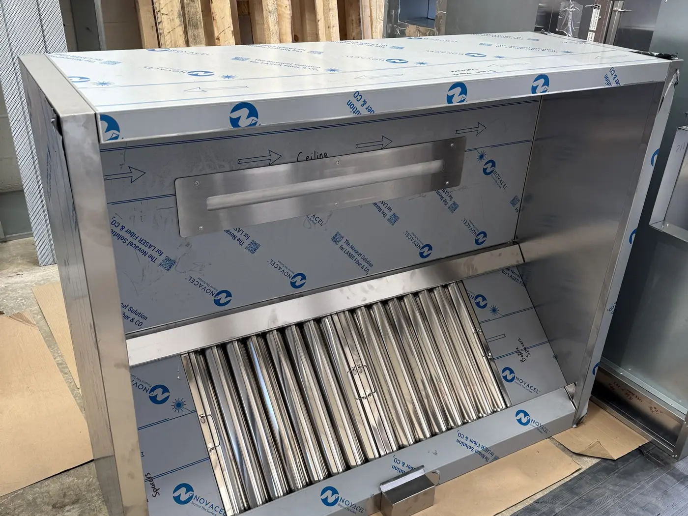 Newly fabricated stainless steel canopy with baffle filters and integrated lighting, still in protective film, in the REAL Ventilation workshop